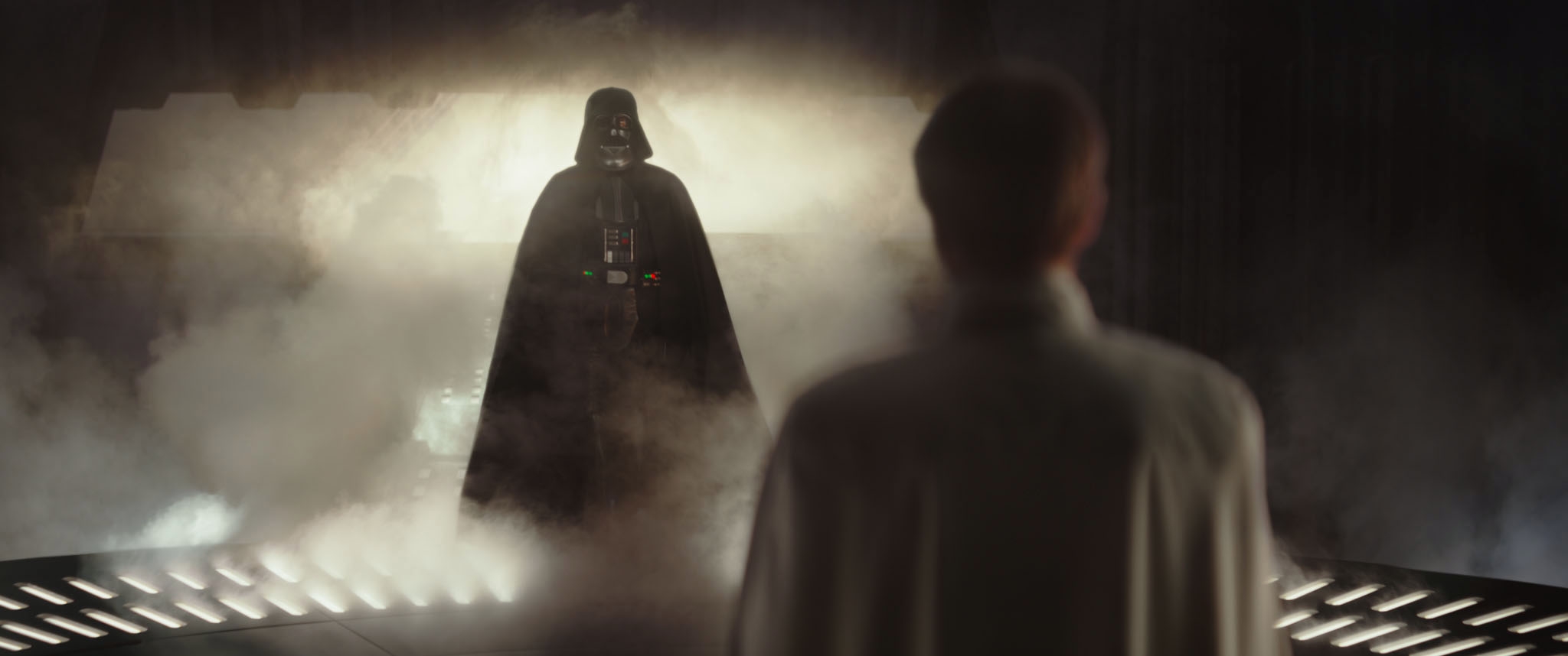 Darth Vader stands in a misty, dimly lit room facing a person in a white coat, evoking a dramatic, tense atmosphere from star wars
