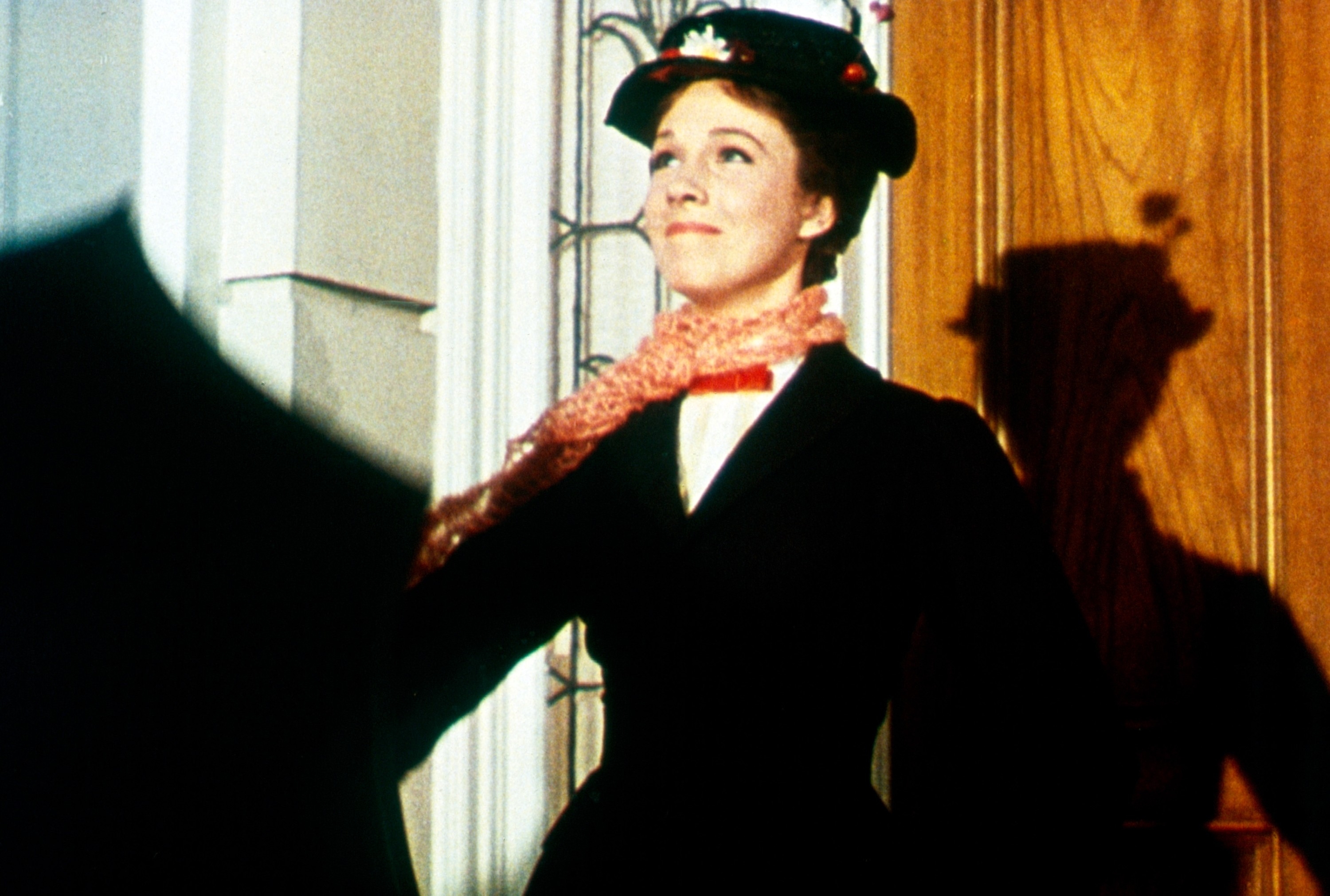 Julie Andrews as Mary Poppins dressed in a vintage outfit with a hat and scarf, standing with an umbrella
