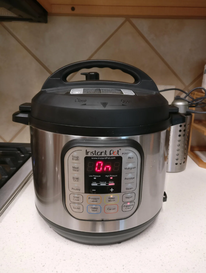 Instant Pot on a kitchen counter displaying "On" with buttons for soup, meat, rice, and more