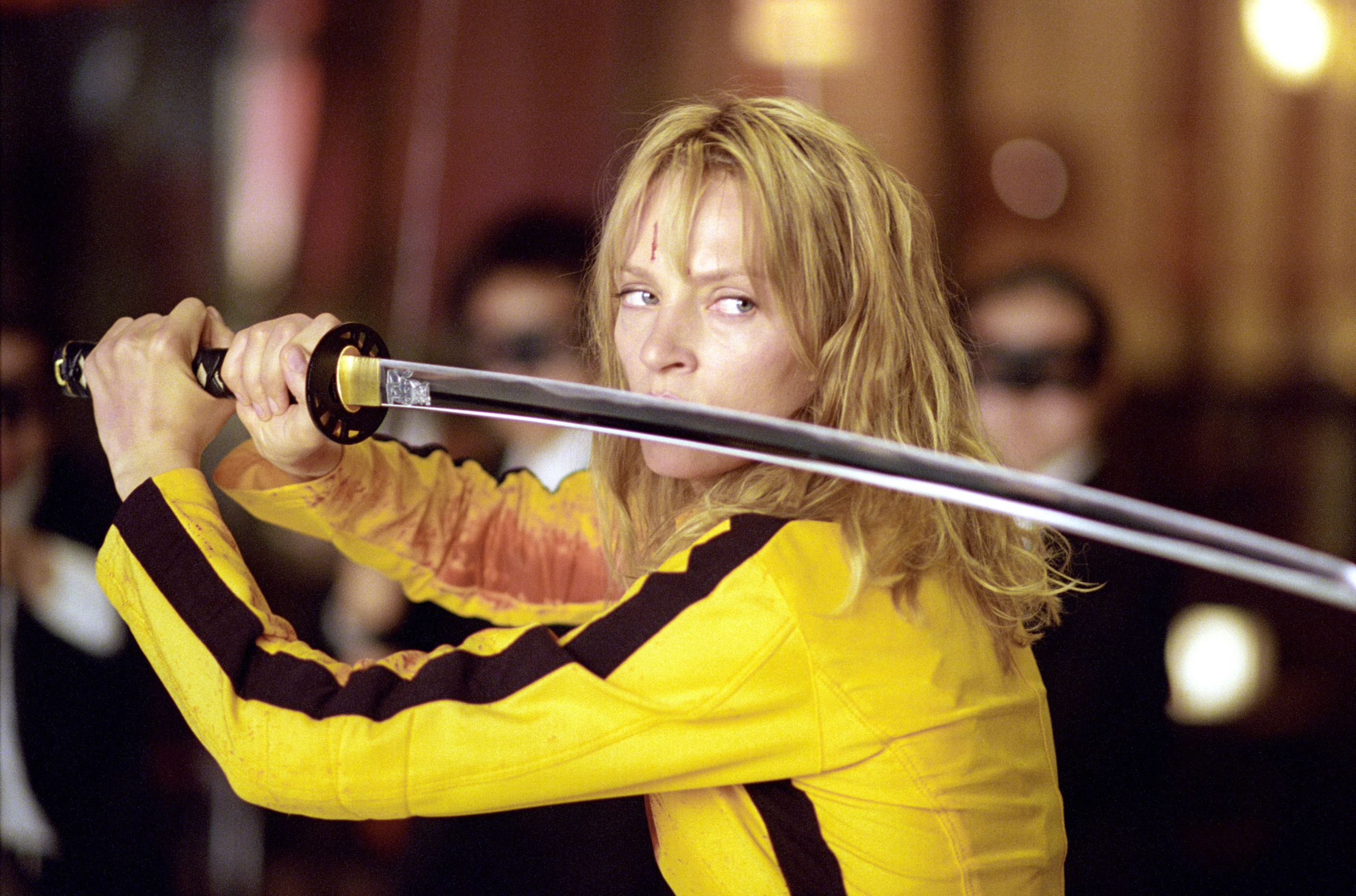 Uma Thurman in a yellow outfit holds a katana in a defensive stance, in a scene from Kill Bill