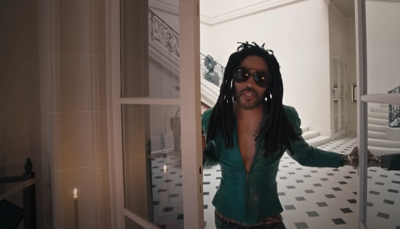 Person standing in an open doorway wearing sunglasses and a stylish fitted jacket