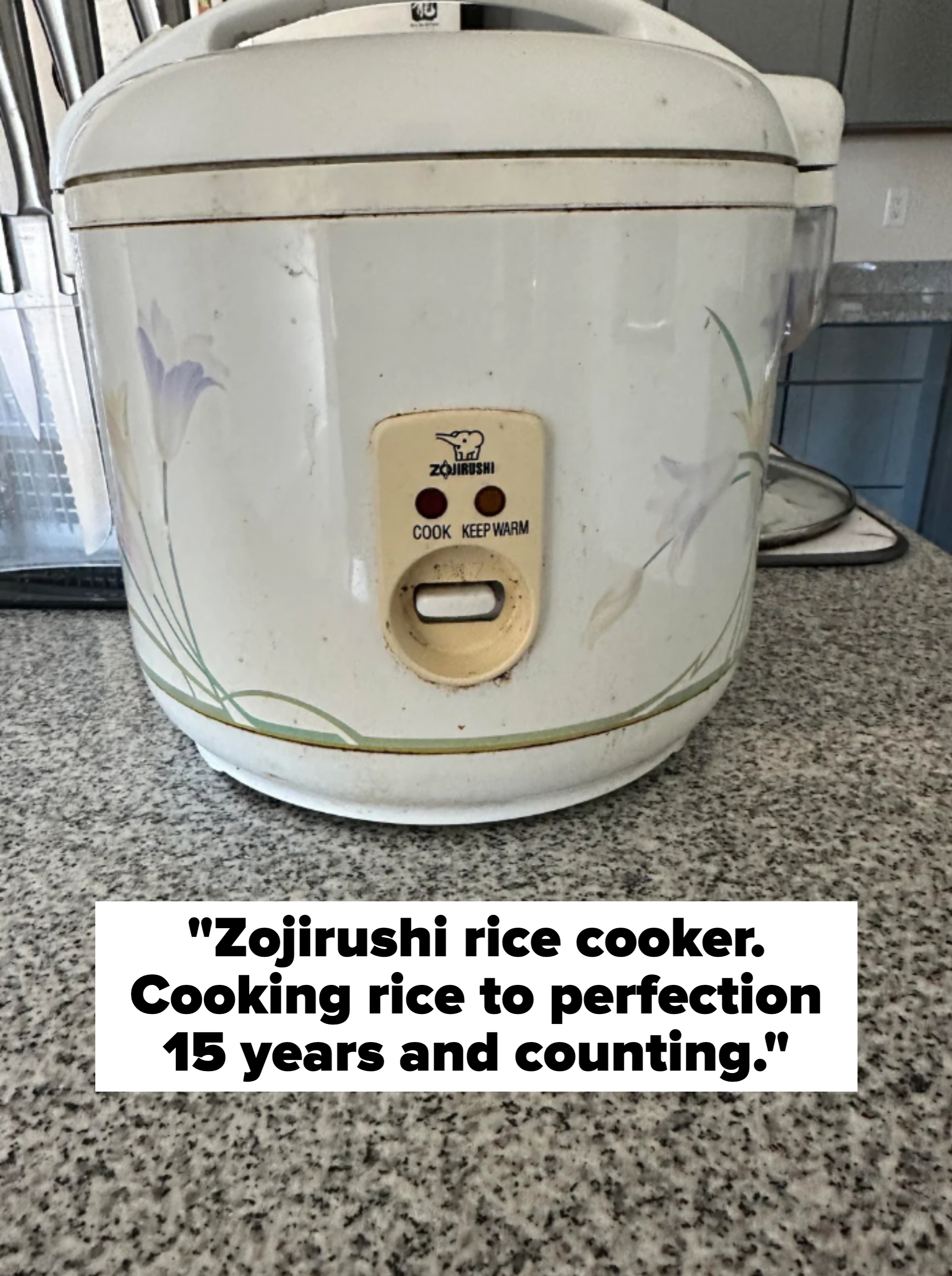 A Zojirushi rice cooker with floral designs on a countertop, showing “Cook” and “Keep Warm” settings