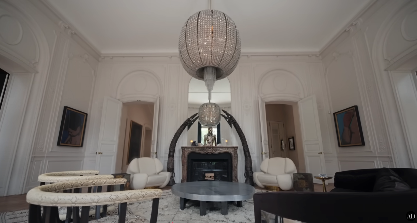 A luxurious living room with elegant chandeliers, modern furniture, and a large, ornate mirror above the fireplace