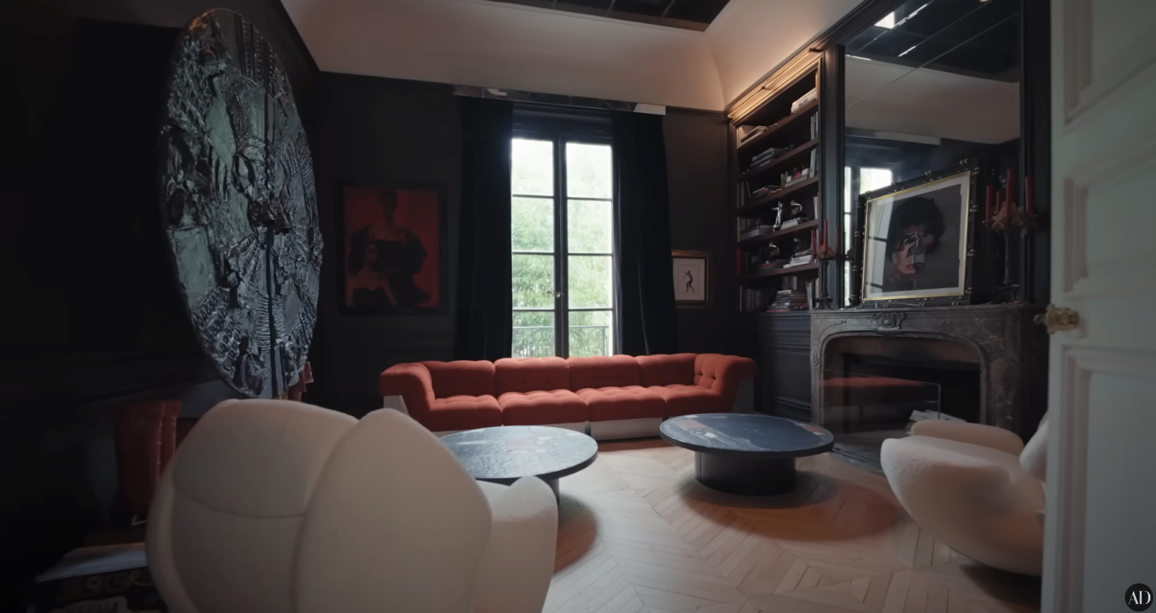 Modern living room with a red sofa, circular chairs, large wall art, and a fireplace with a mirror, creating a stylish and elegant atmosphere