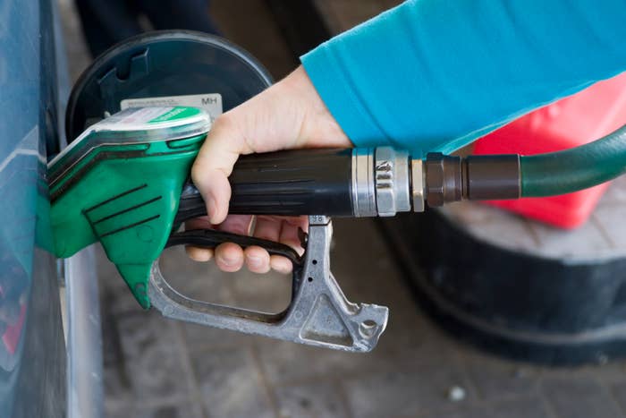 Person refuels vehicle at gas station, holding green fuel nozzle into car's fuel tank