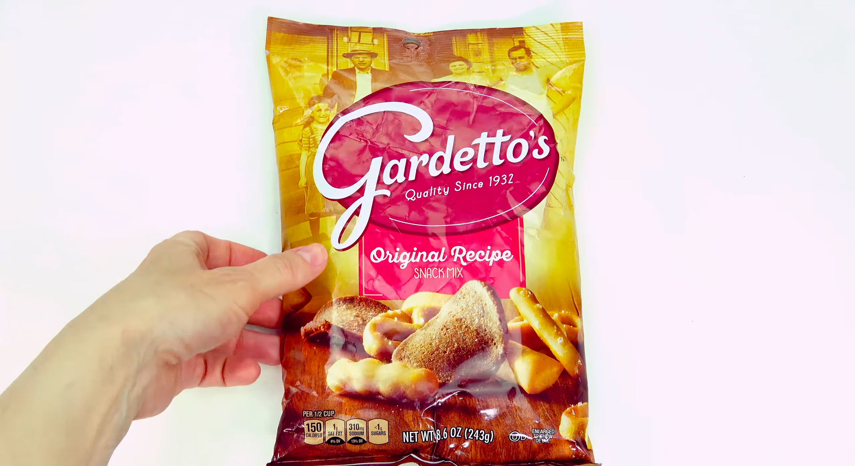 A hand holds a bag of Gardetto's Original Recipe snack mix against a plain background