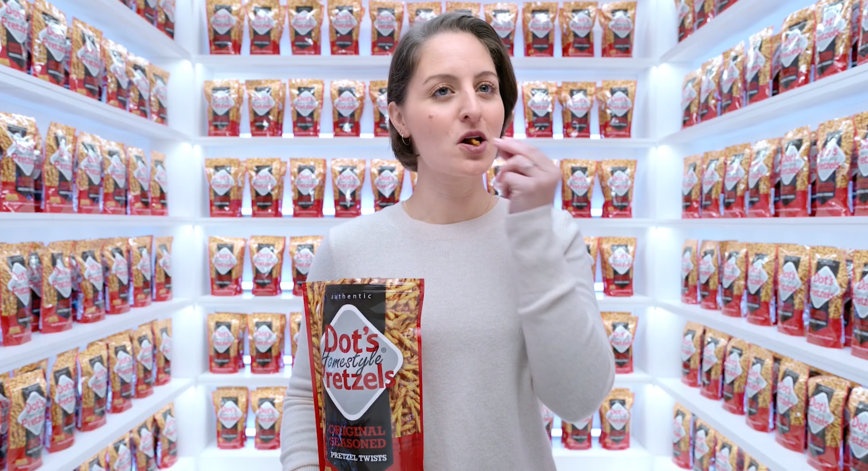 Person eating Dot's Pretzels in a room full of pretzel bags. They wear a simple long-sleeve top