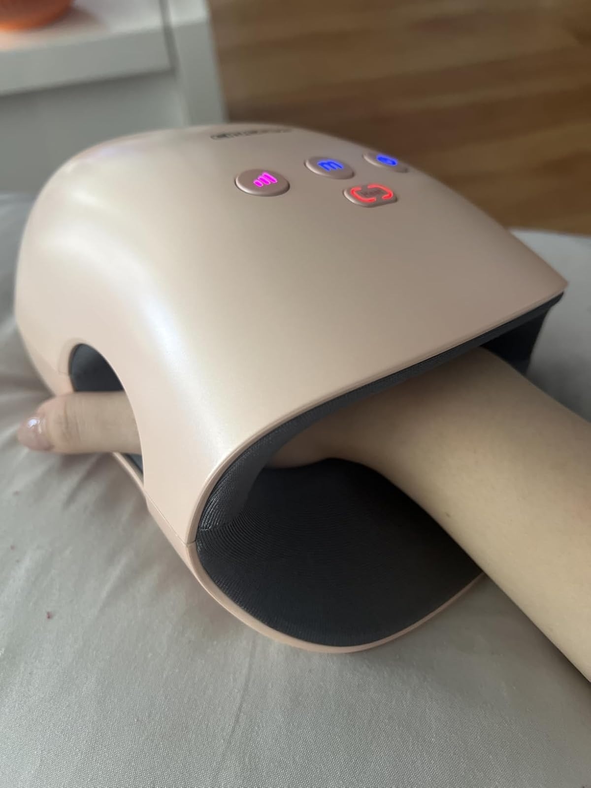 Reviewer hand using a hand massager with LED display and buttons on top, placed on a cushion