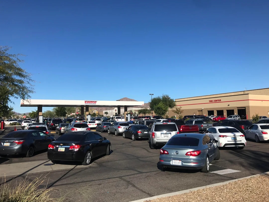 Busy Costco gas station with many cars lined up, adjacent to a tire center, indicating high demand and bustling activity