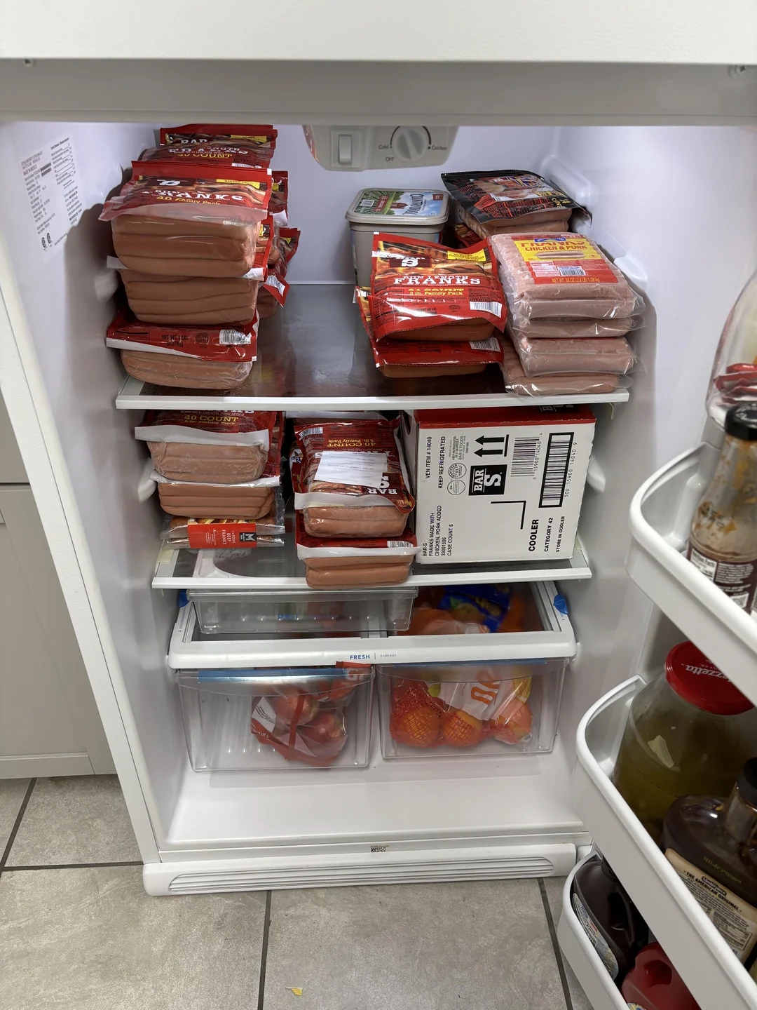 A refrigerator filled with packaged hot dogs, a small box, and various jars on the door shelves