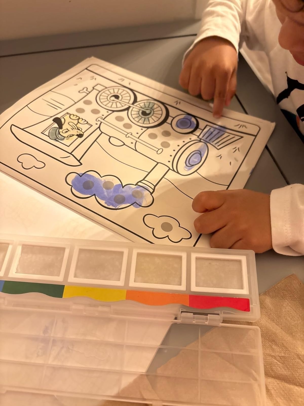 Child painting a picture of a train with a watercolor set, using fingers to fill in details
