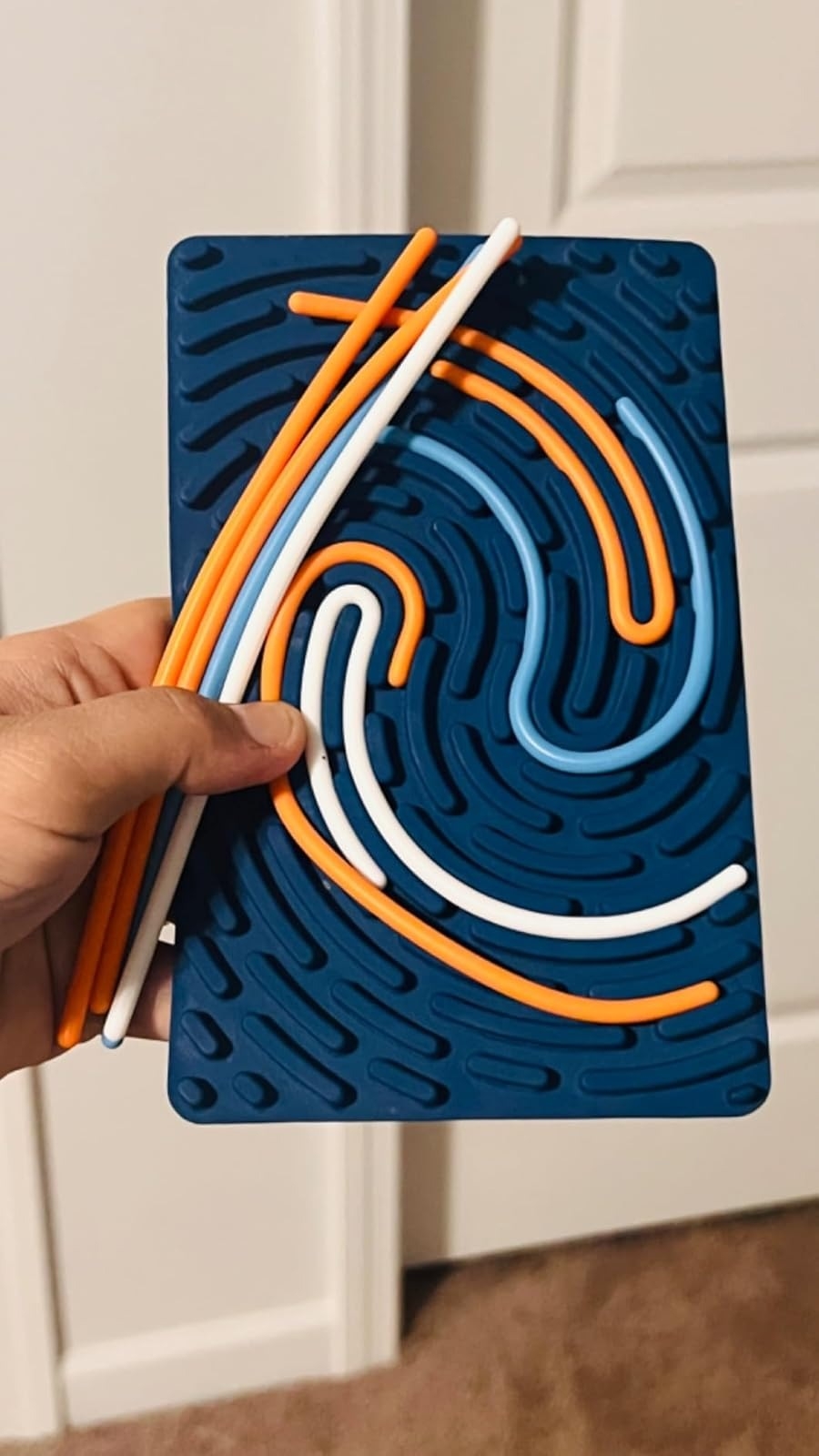 A hand holds a puzzle toy with grooved patterns and removable flexible rods for arranging, used for stress relief and creativity