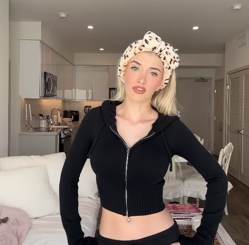 Person in a modern kitchen, wearing a black zip-up top and a patterned headband, posing with hands on hips
