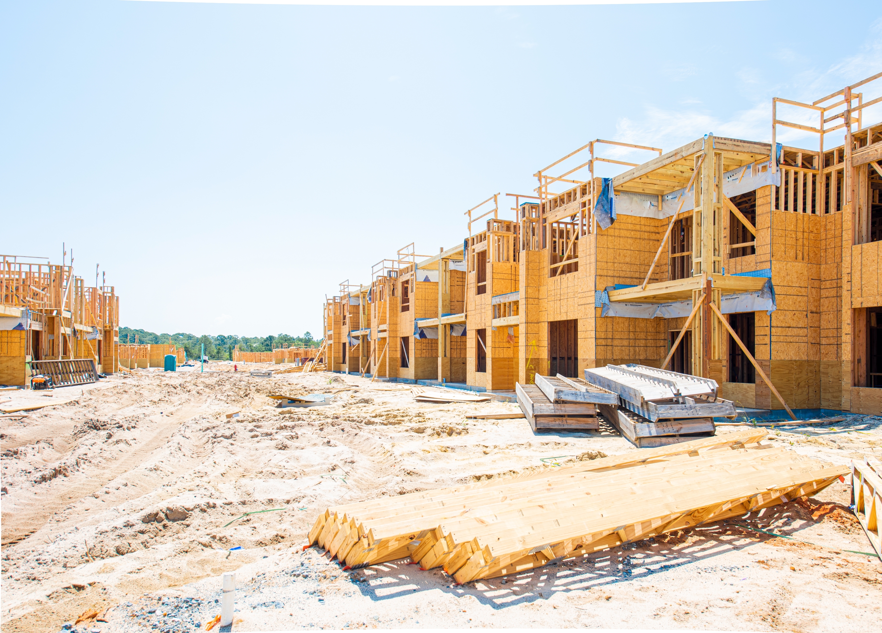 Construction site with partially built wooden structures, framing a future residential area under clear skies
