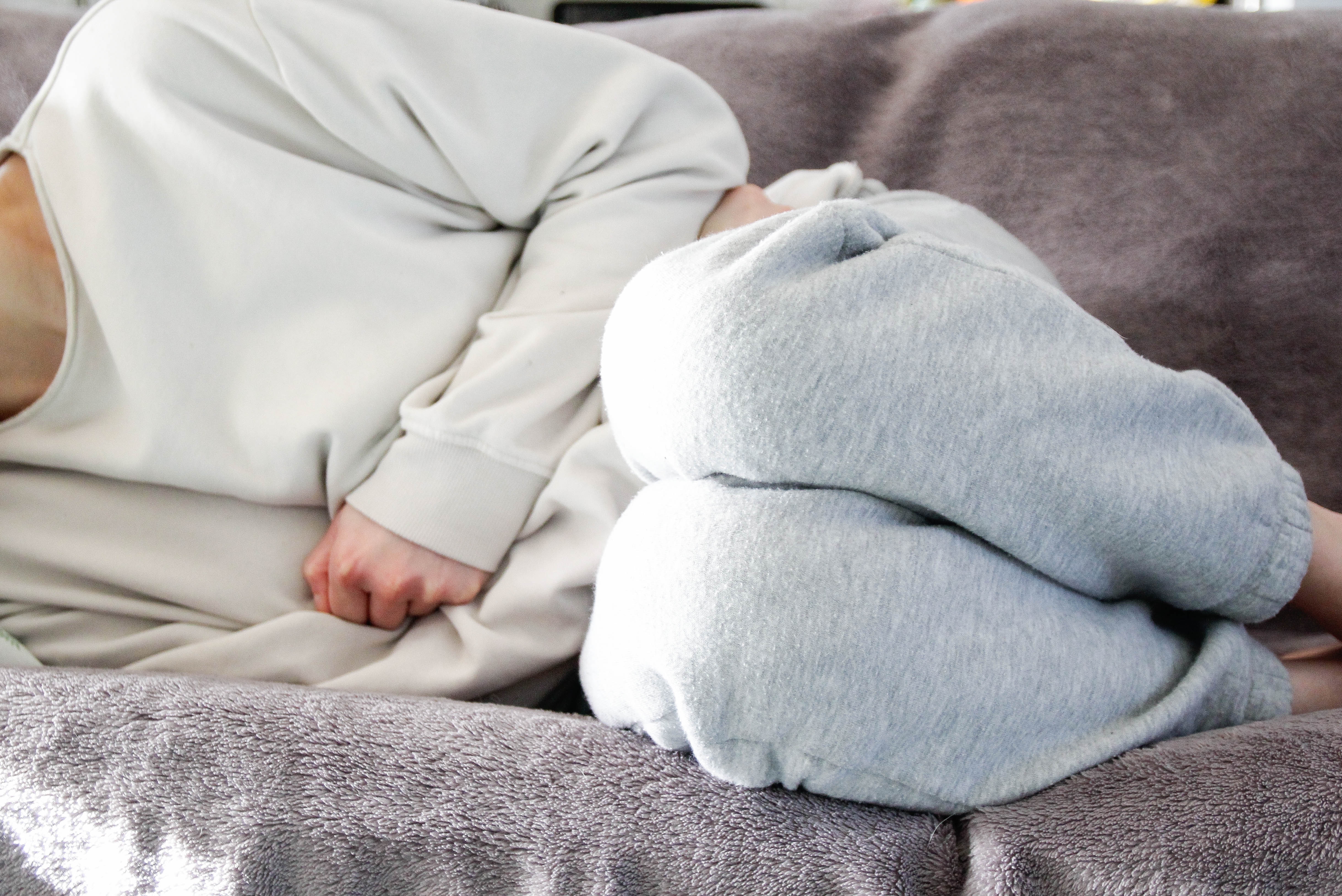 Person in cozy loungewear is lying on a couch, curled up and resting