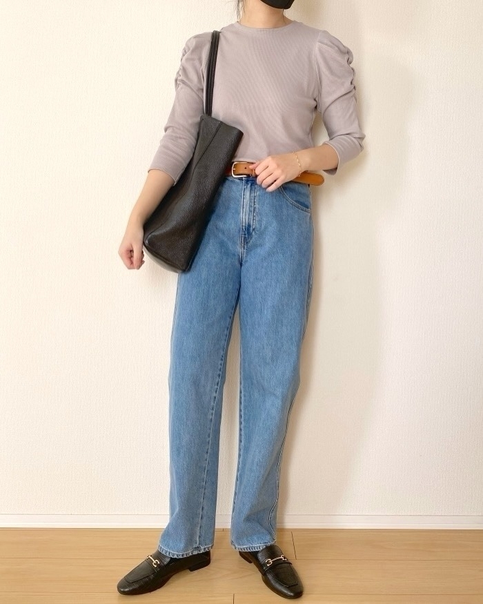 女性がリラックスしたトップスにデニムパンツを着用し、黒のトートバッグを肩にかけている。カジュアルな装い。