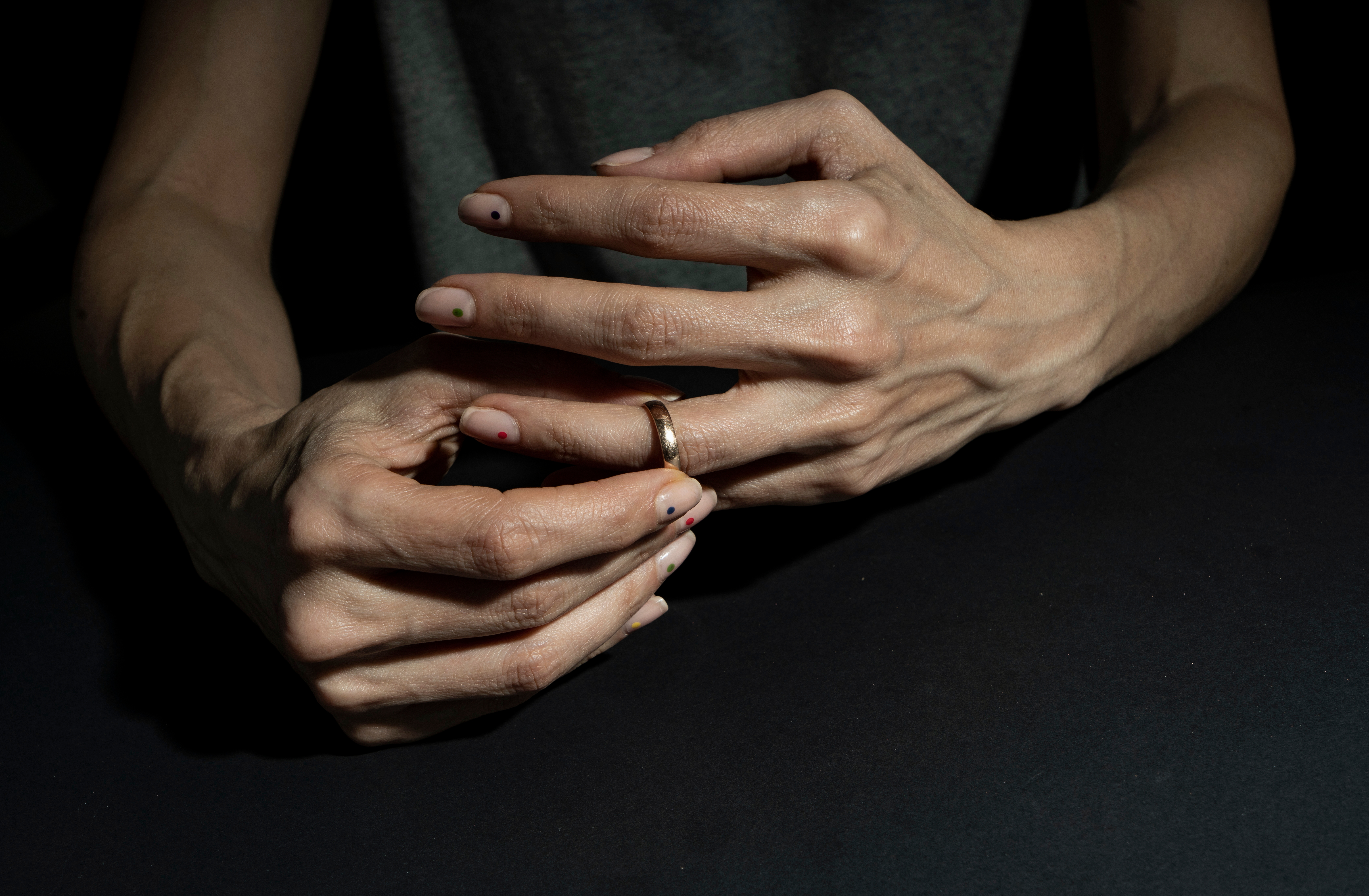 Person's hands resting on a table, wearing a ring on one finger, with nails painted with small designs