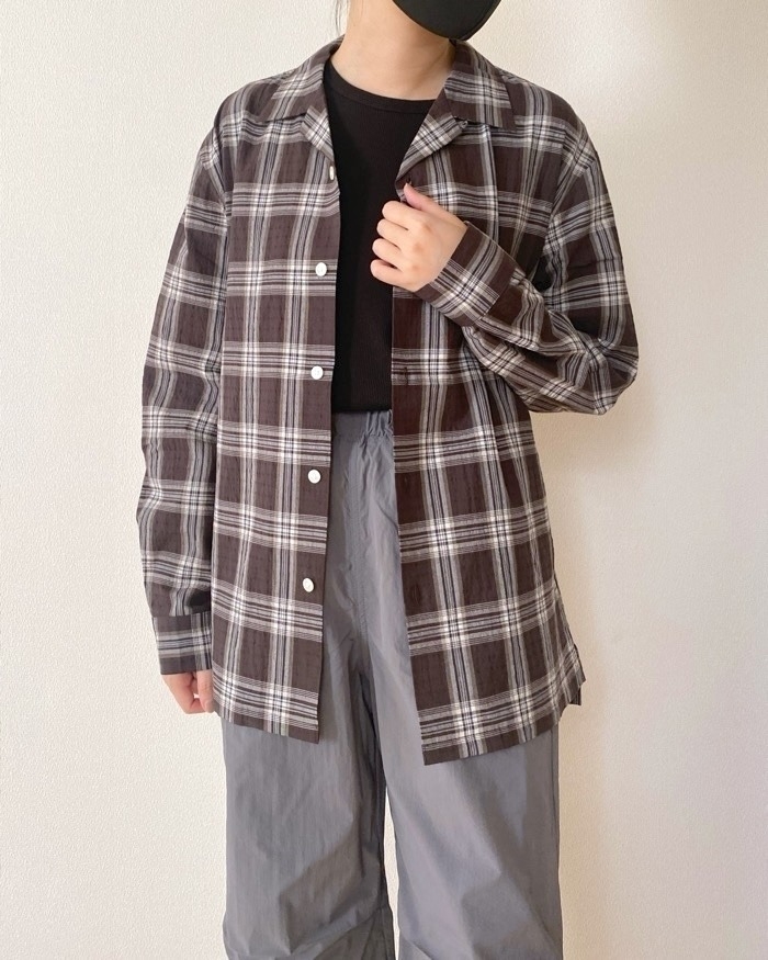 チェック柄シャツとゆったりとしたパンツを着た人物がマスクを着用して立っている。