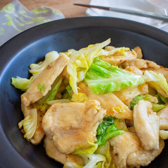 皿に盛り付けられた焼いた鶏肉とキャベツの料理。背景に箸と皿。