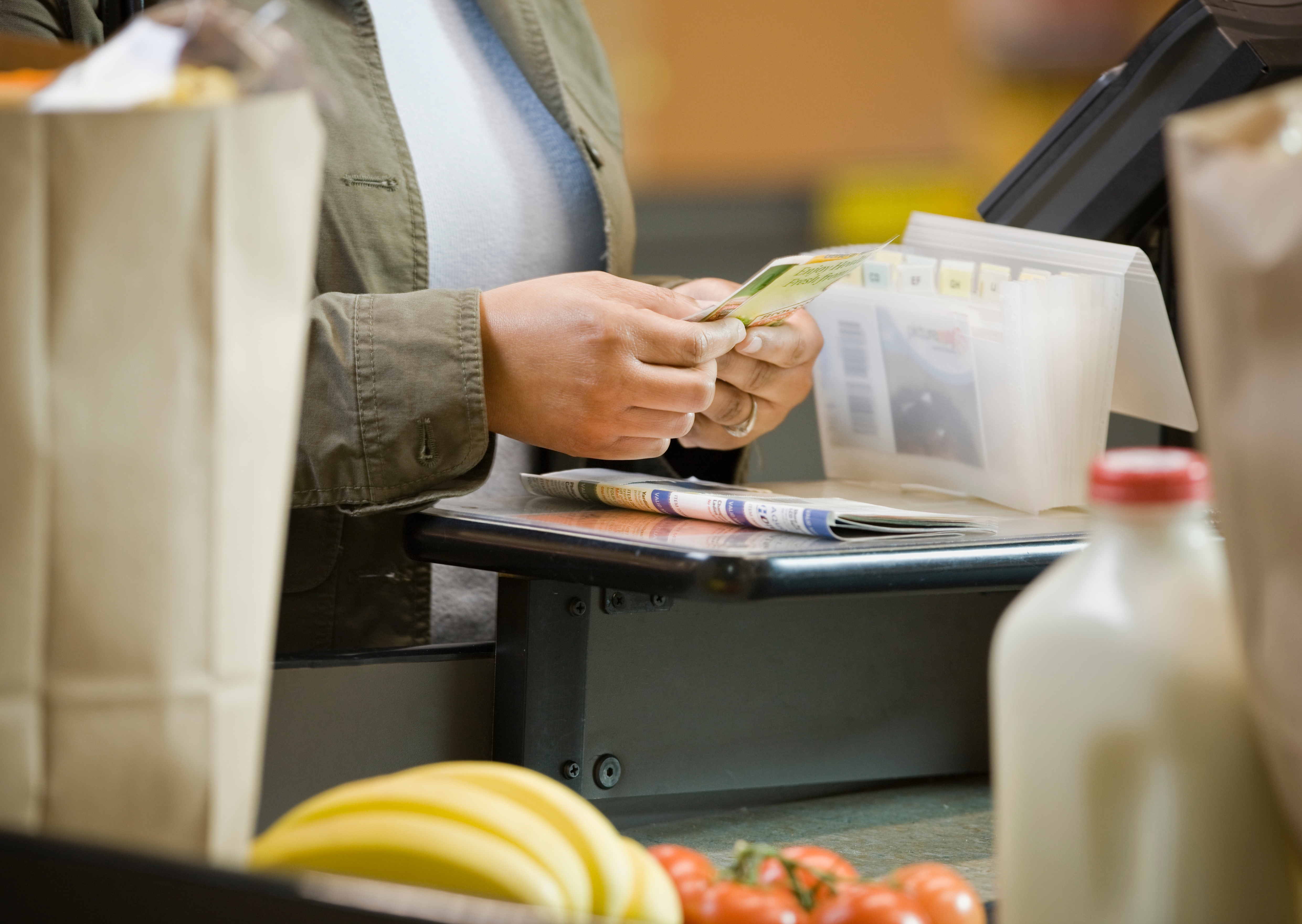 Person at a checkout counter placing cash on the counter, with groceries including bananas and tomatoes in the foreground