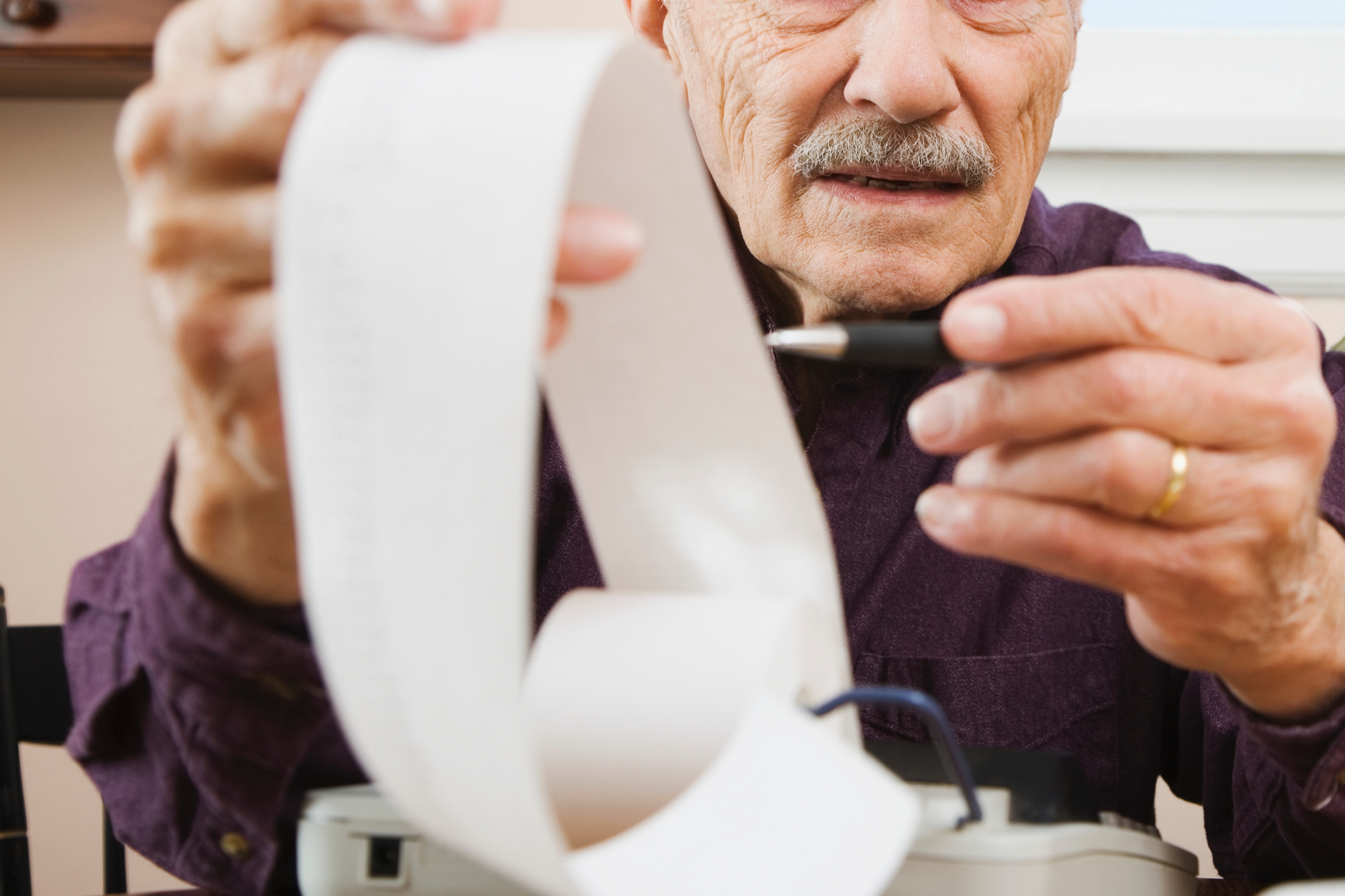 Elderly couple reviewing a long receipt with a calculator, appearing concerned. Woman is resting her head on her hand