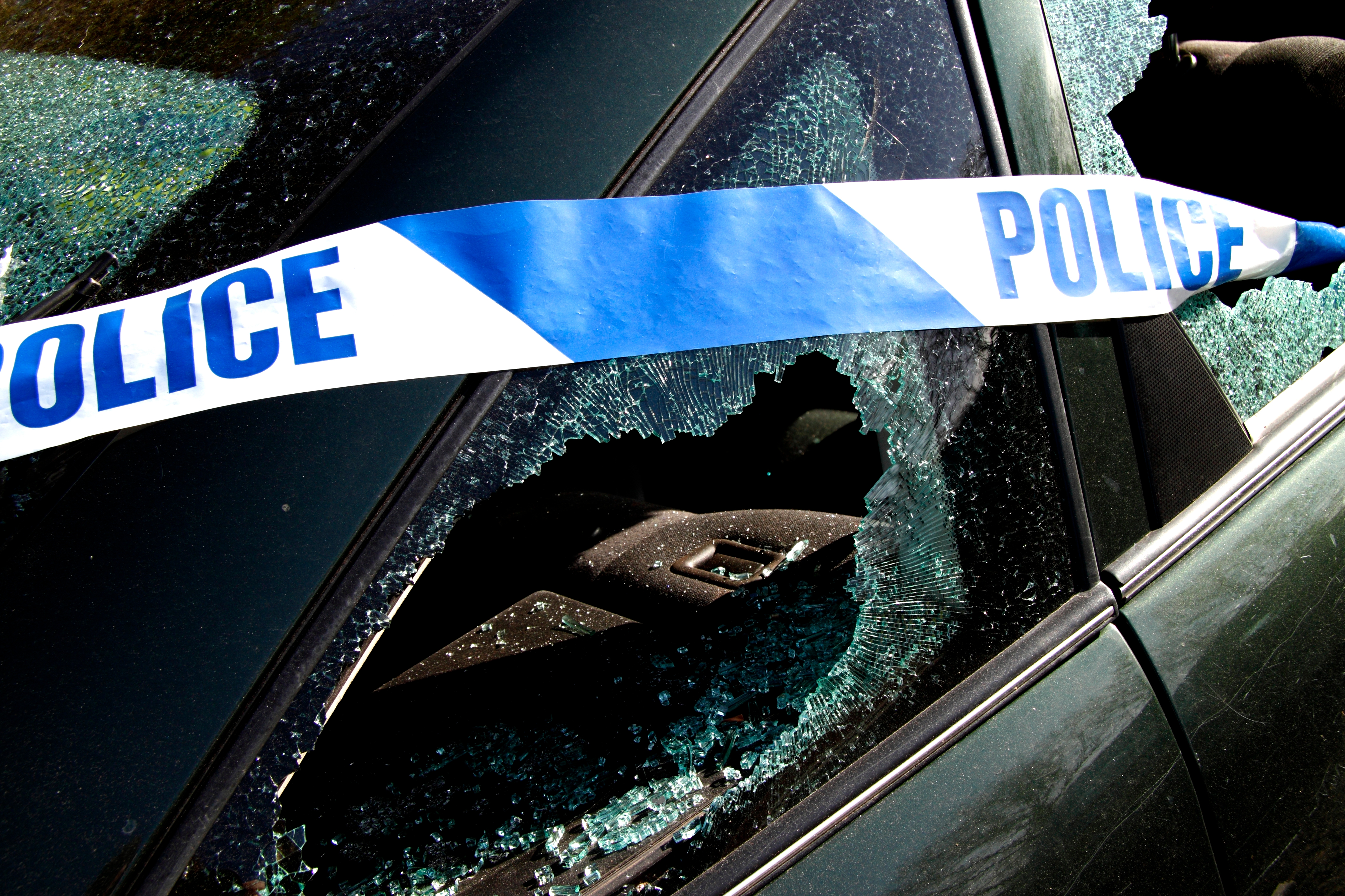 Car with a shattered window, police tape draped across, indicating an incident or investigation in progress