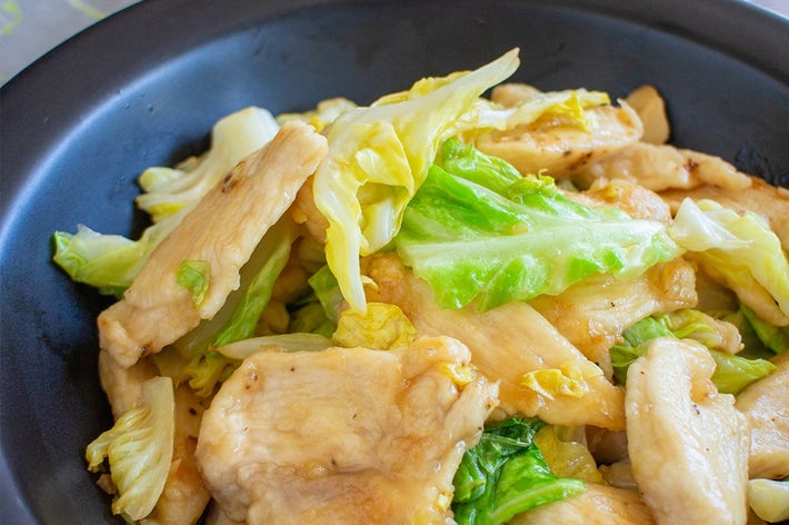 お皿に盛られたキャベツと鶏肉炒め。背景に箸と白い皿が見える正面ショット。