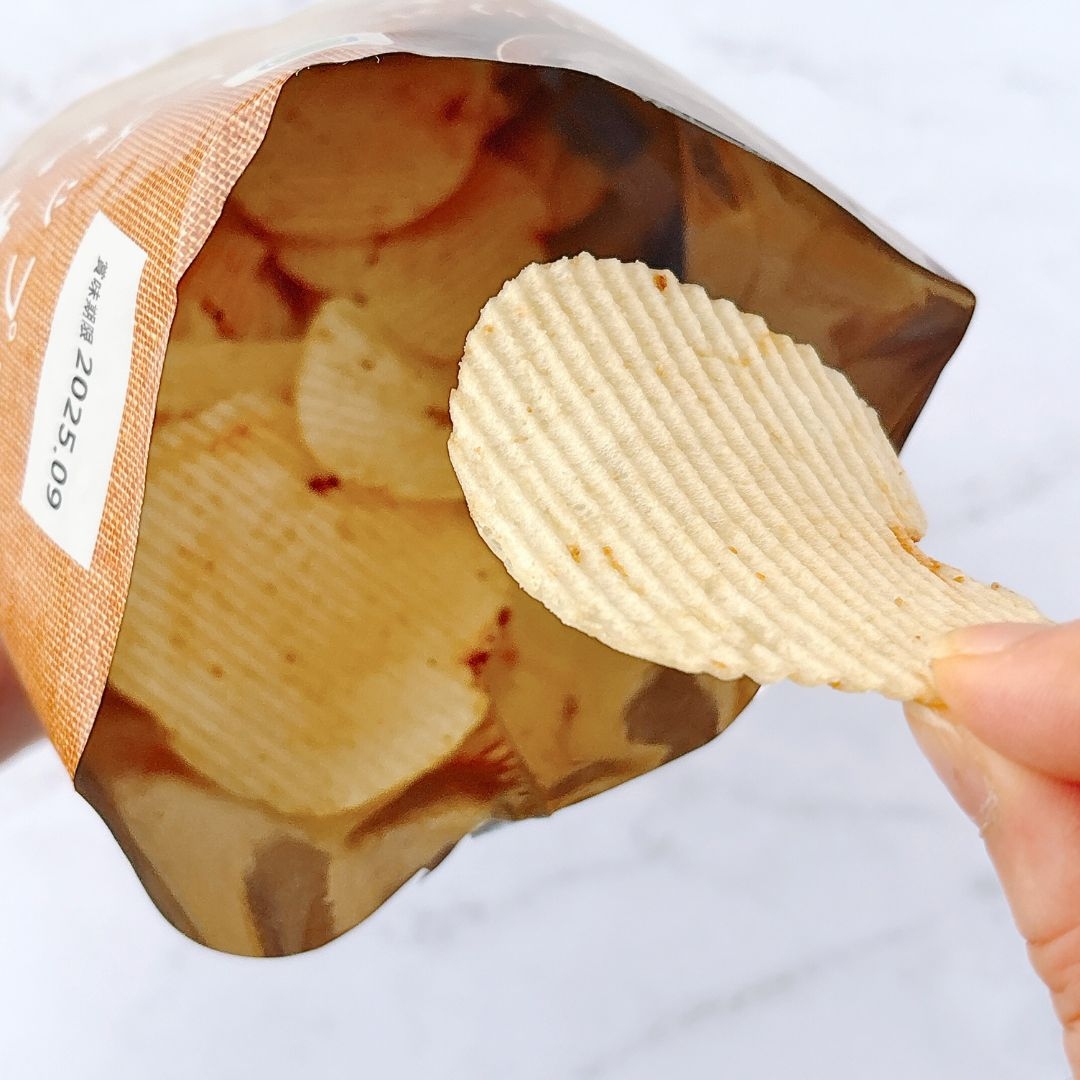 袋から取り出されたポテトチップスを持つ手。袋の中にはまだチップスが多く見える。