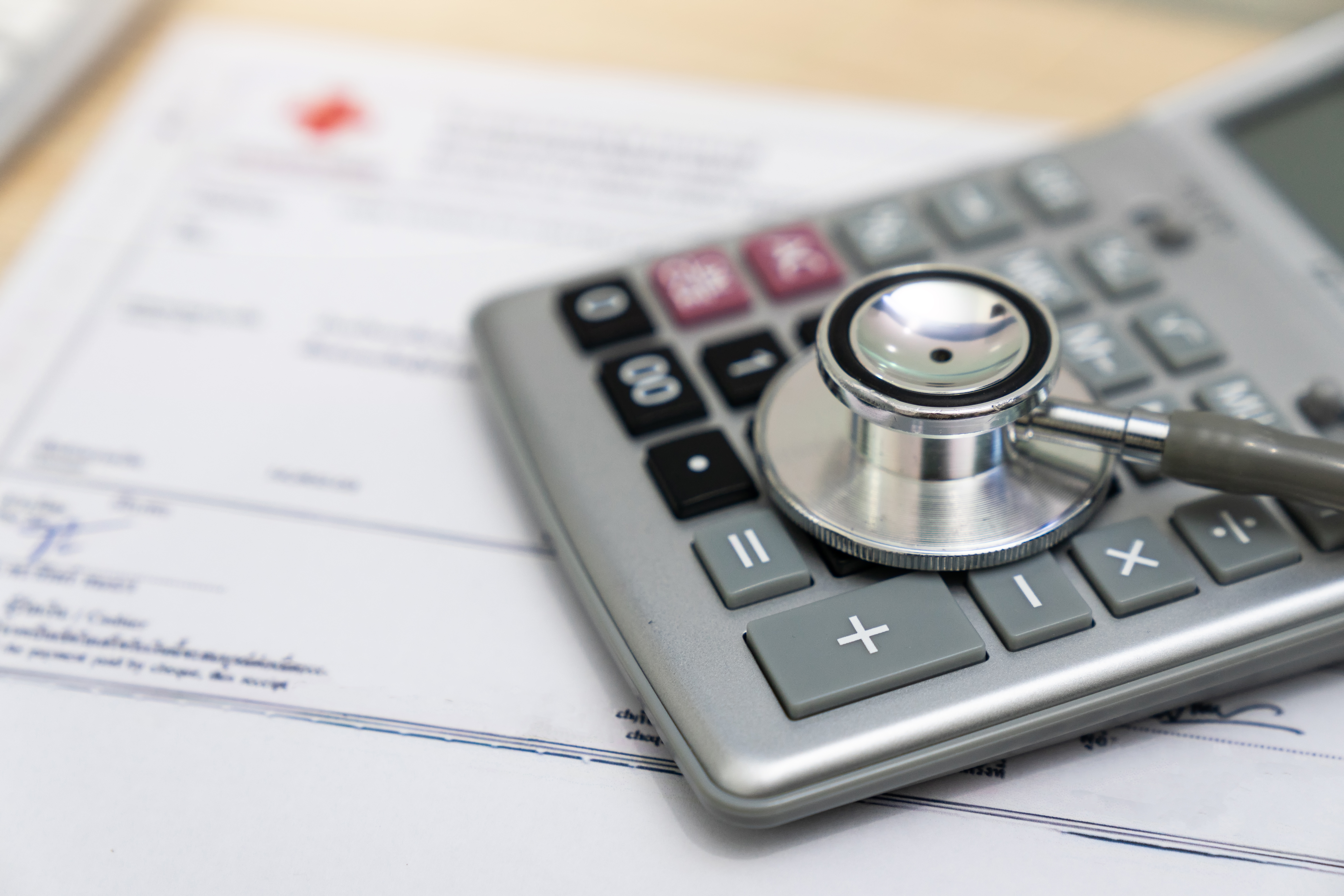 Stethoscope on a calculator resting on documents, symbolizing healthcare costs and financial planning