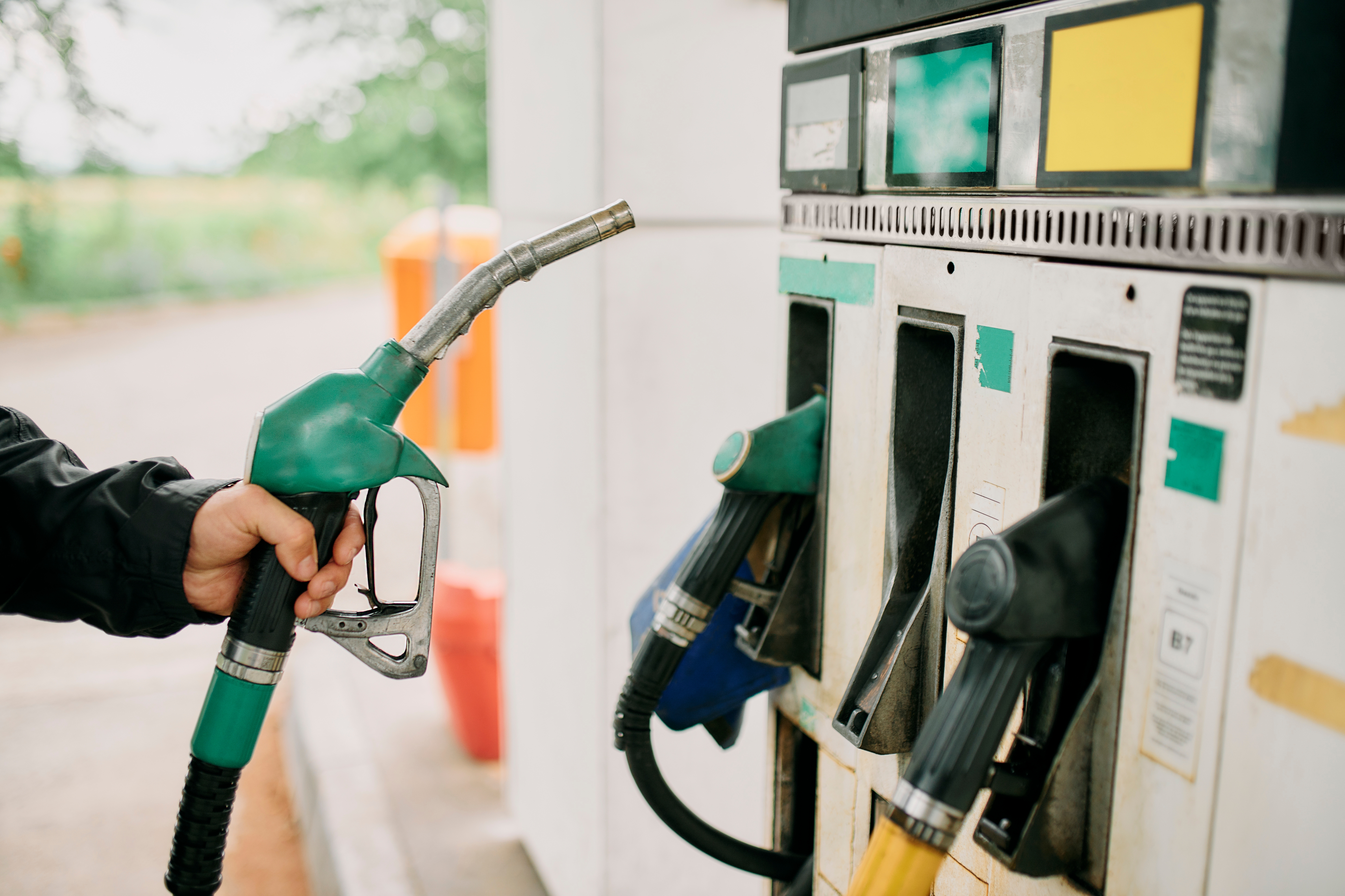 A person holds a fuel nozzle near a gas pump, selecting between multiple fuel options at a station