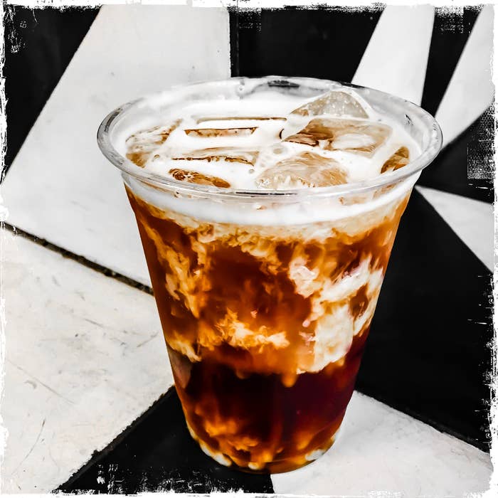 Iced coffee with milk in a clear plastic cup against a geometric backdrop