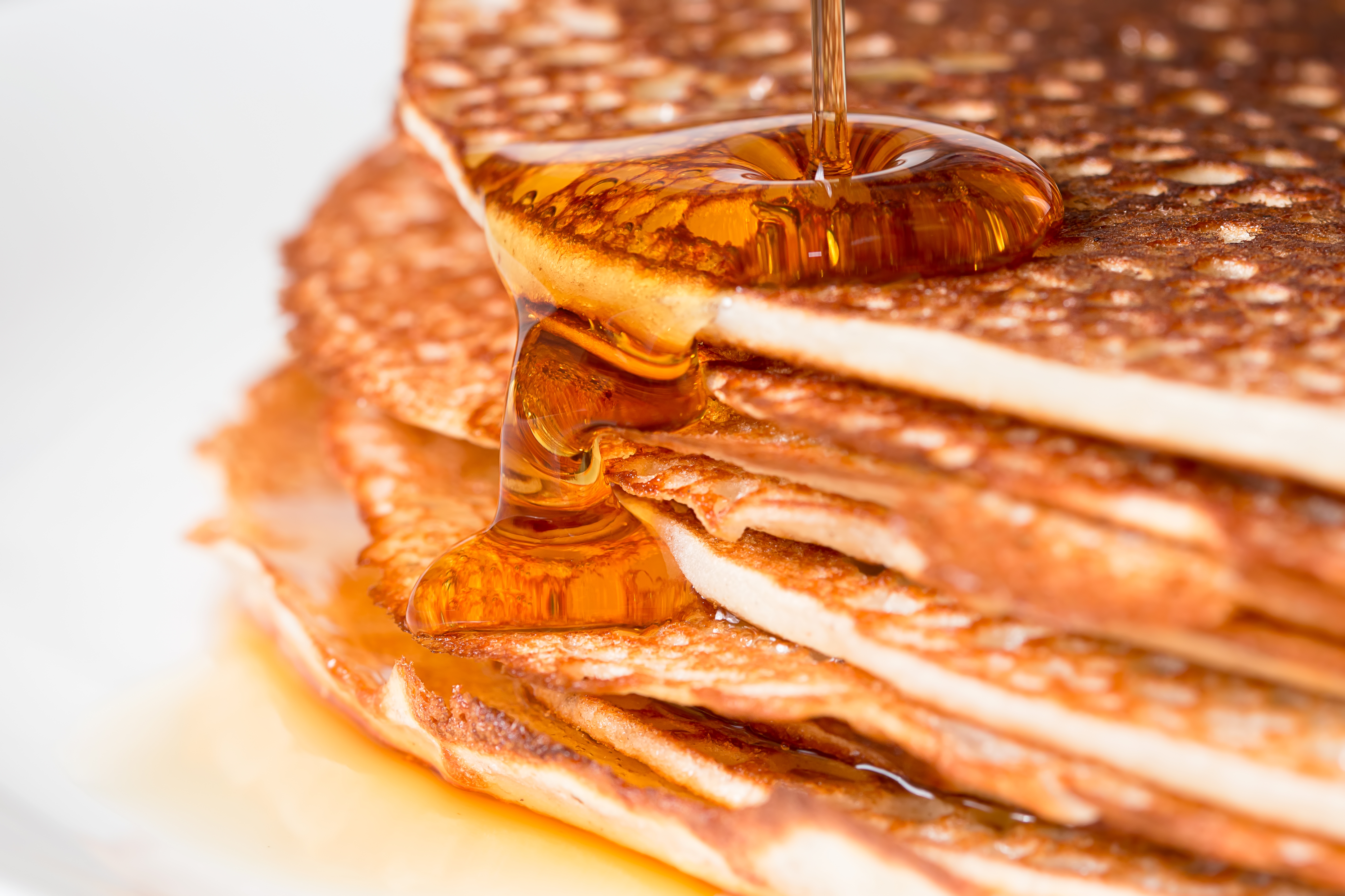 Close-up of syrup being poured over a stack of pancakes, highlighting texture and richness