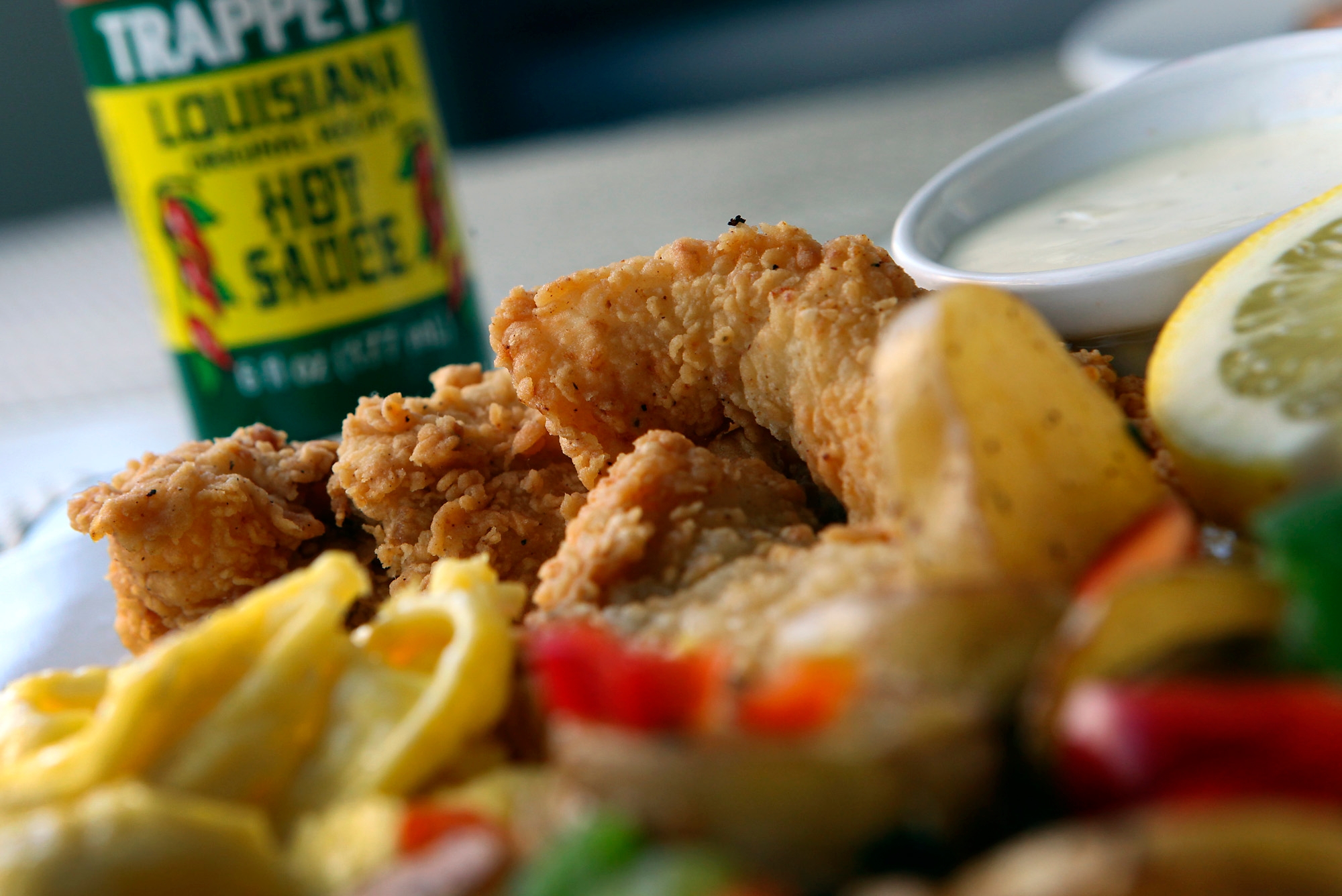 Plate of fried chicken, lemon slice, scrambled eggs, and vegetables with a bottle of hot sauce in the background