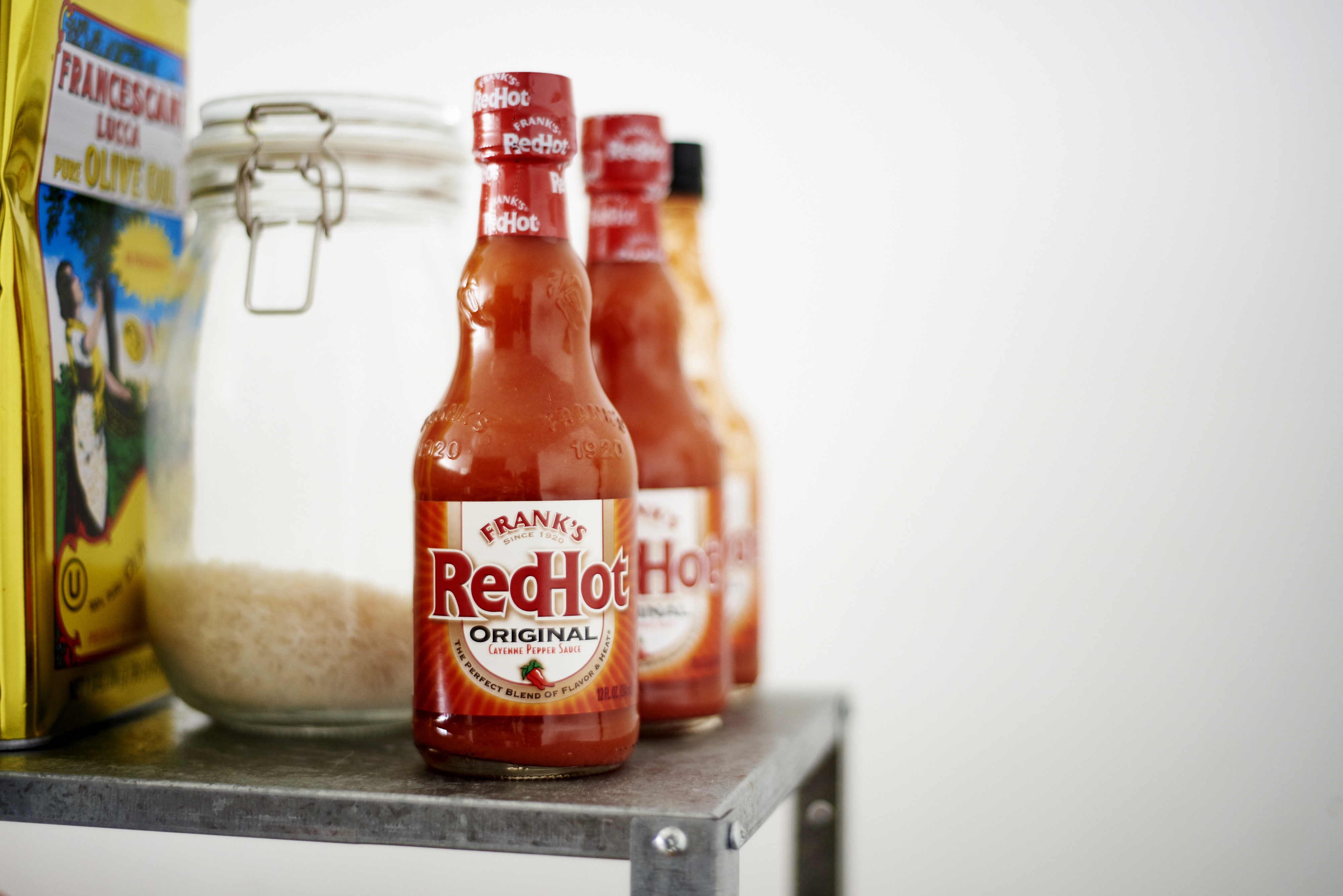 Hot sauce bottles and a jar of rice are arranged on a metal shelf, with a cereal box nearby