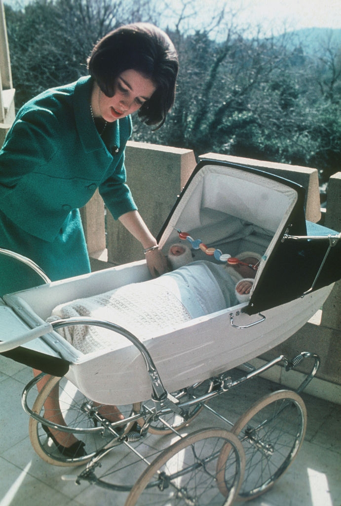 Woman in elegant coat tending to a baby in a vintage pram outdoors