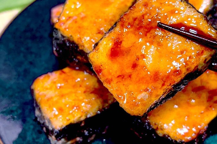 お皿に盛られた3つの照り焼き風グレーズがかかった豆腐寿司。箸で一つを持ち上げている。