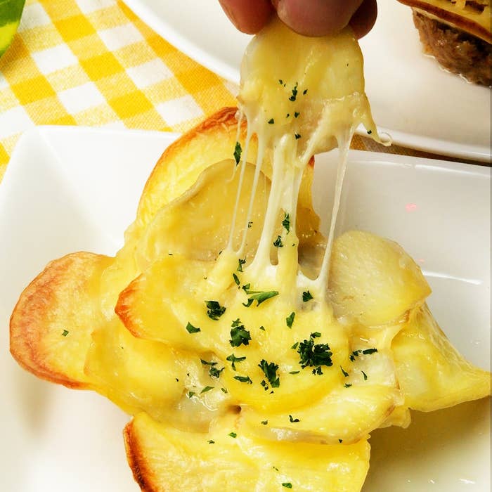 チーズがとろけたポテトグラタンを人が一切れ持ち上げている様子。