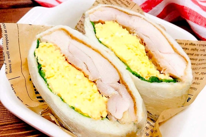 サンドイッチの断面。卵サラダ、チキン、野菜入り。背景に赤と白のストライプの布がある。