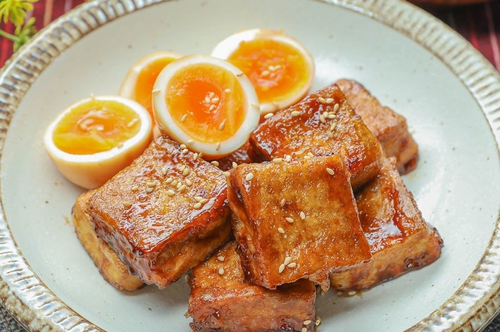 皿に盛られた照り焼き風の厚揚げと半熟卵。背景に植物とスープ。
