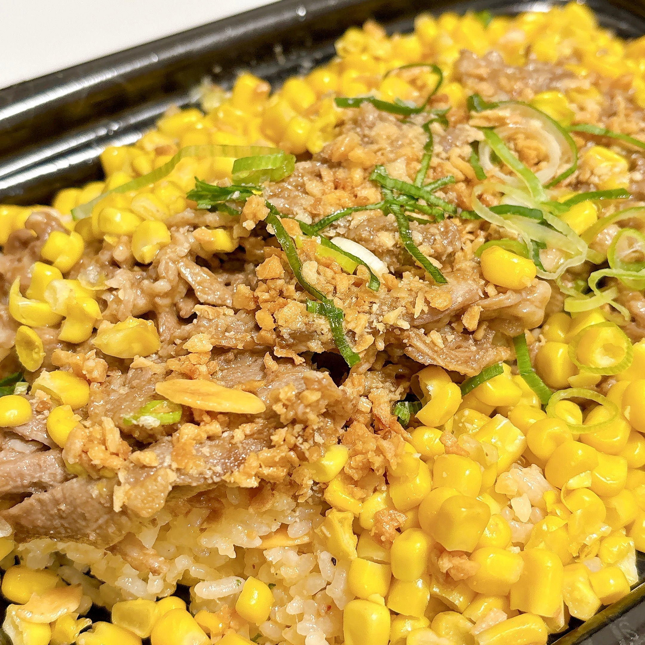 コーンと薄切り肉が乗った米の上の料理。ネギがトッピングされている。