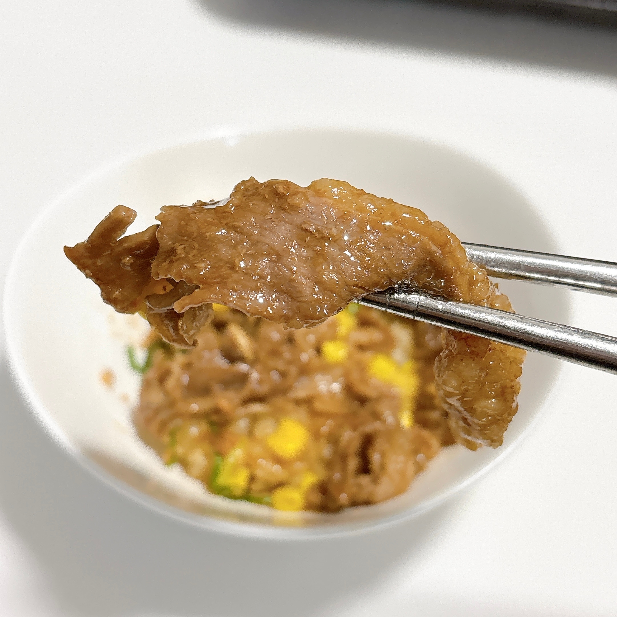 白いボウルに入った牛丼。箸で持ち上げられた一切れの肉が手前に見える。
