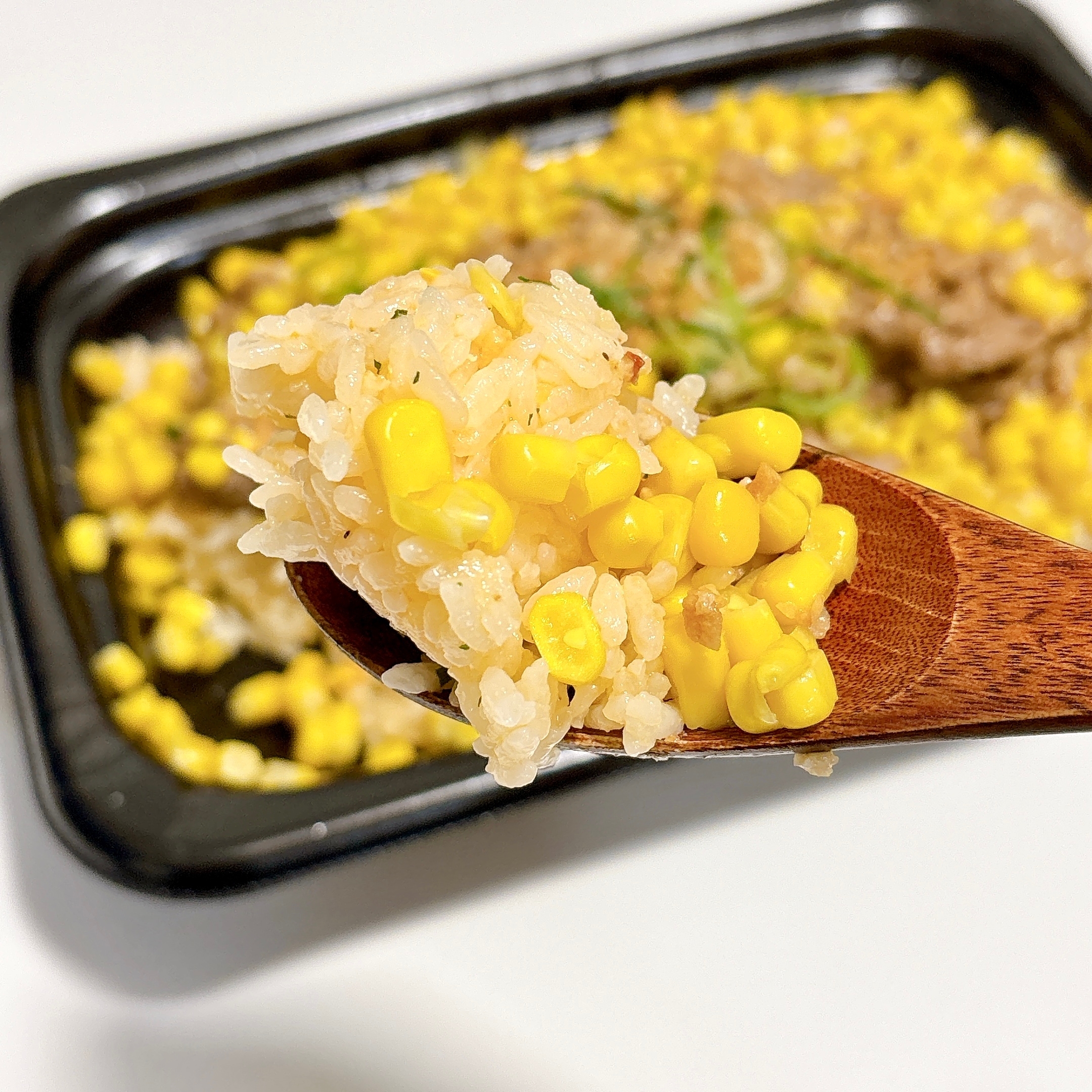 スプーンに盛られたコーン入りのご飯をクローズアップした画像。背景に同じご飯が見える。