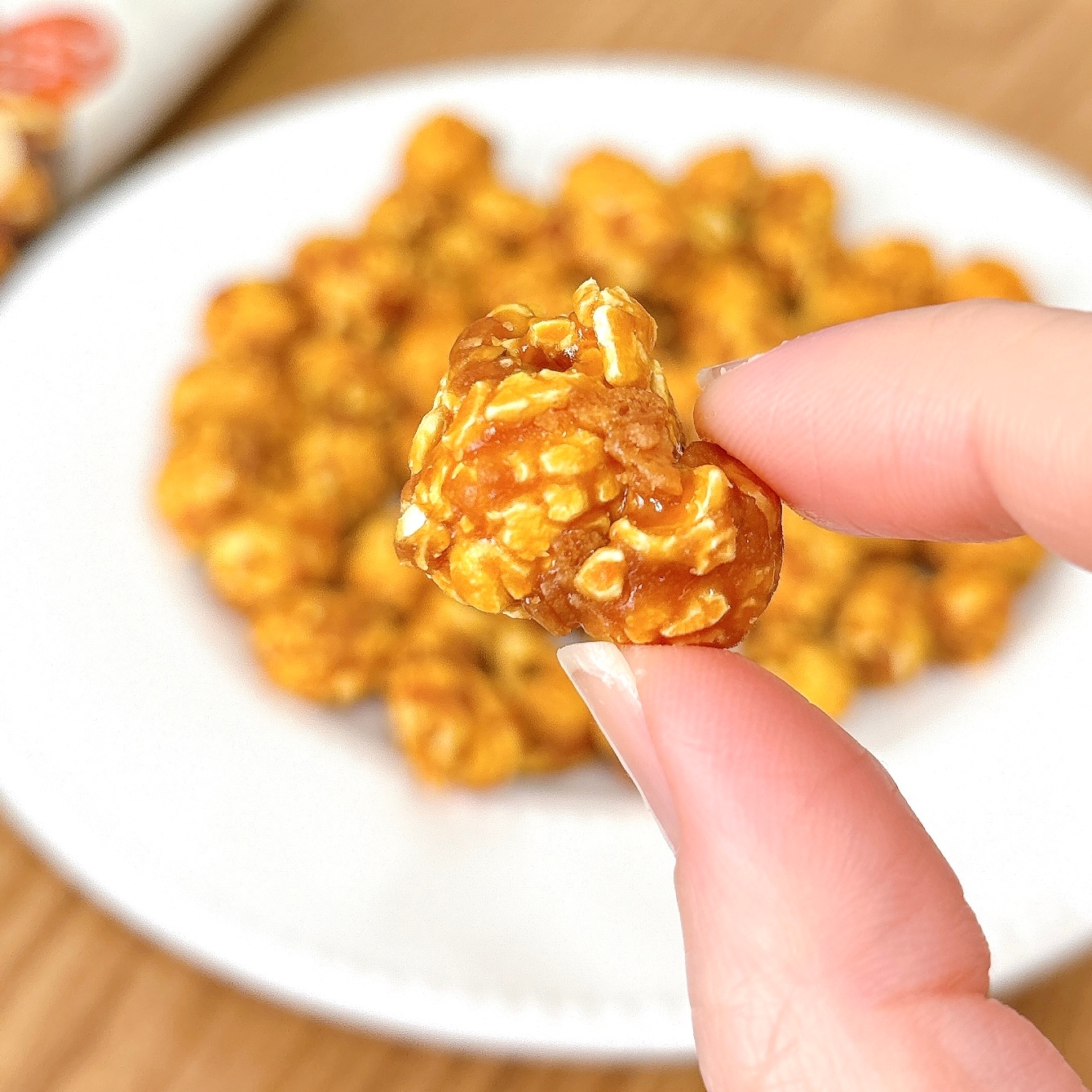 ポップコーンを手に持った画像。背景には皿に盛られた多数のポップコーンが見える。