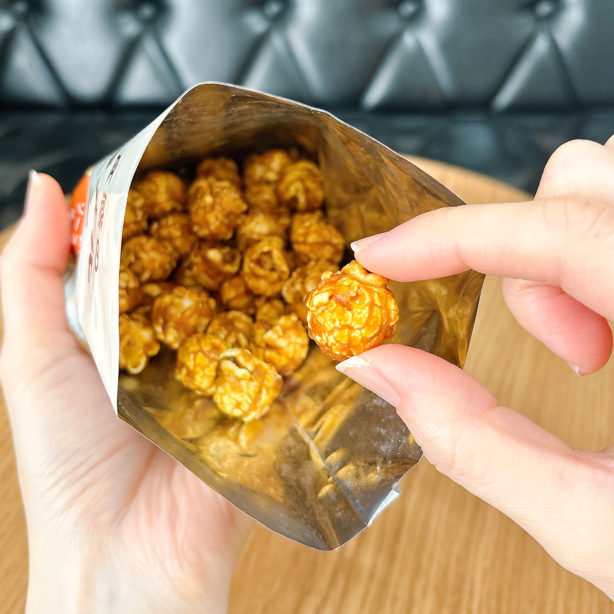 キャラメルポップコーンを袋から取り出す手元のクローズアップ。バックグラウンドはシンプルなソファ。