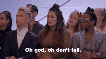 People sitting, one in a green dress, react with concern; overlay text reads, "Oh god, oh don't fall."