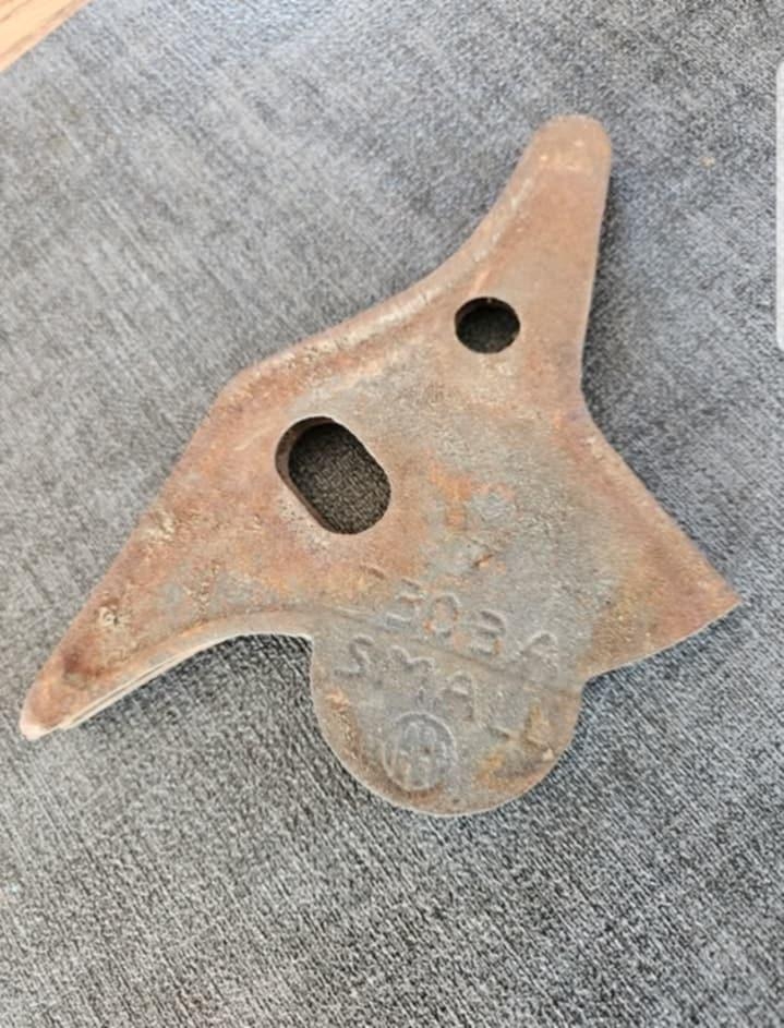 Rusty, triangular metal object with holes and embossed text; appears weathered and worn