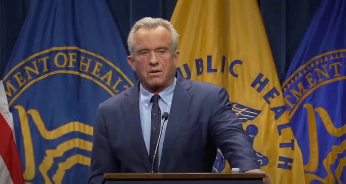 A man in a suit speaks at a podium with Department of Health and Public Health banners in the background