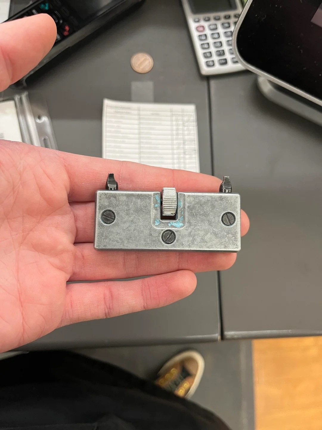 Person holding a metal device with two hooks and a central dial, above a desk with office items