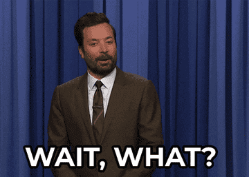 A man in a suit stands in front of a curtain, gesturing with one hand. Text overlay reads, "Wait, what?"