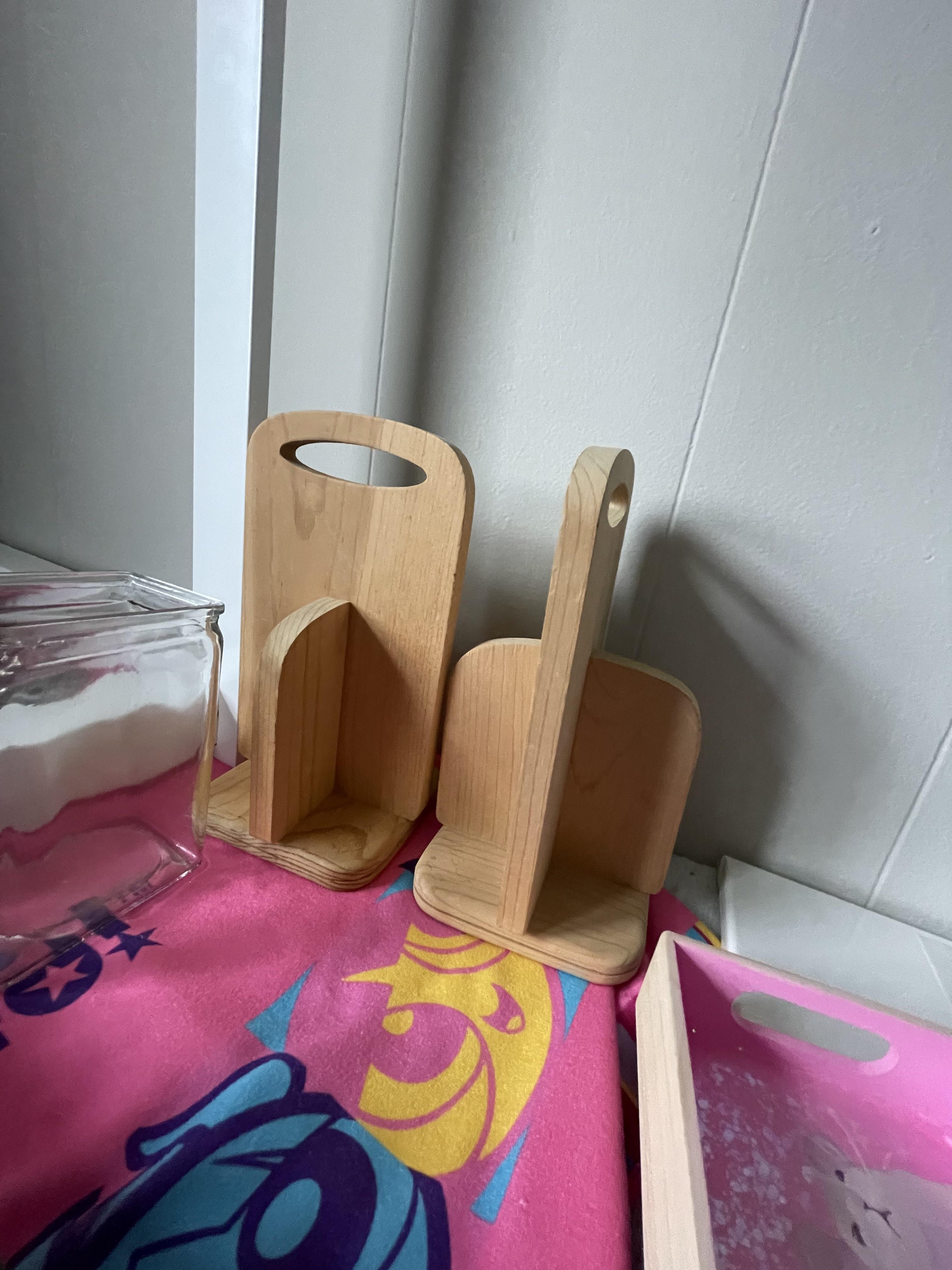 Two wooden cutting boards with handles stand upright on a counter, next to a glass container and a colorful cloth with abstract patterns